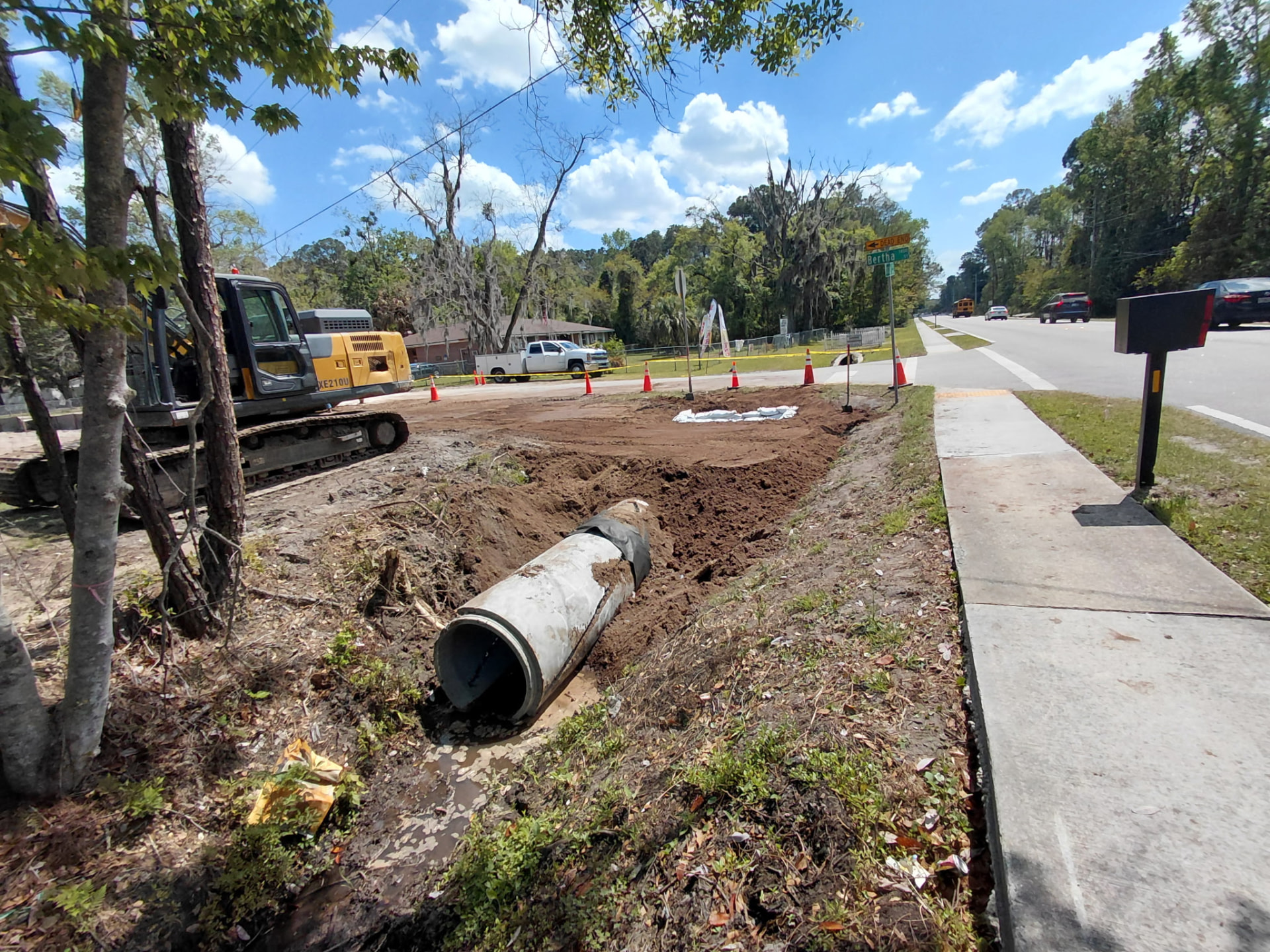 Bertha Street excavation with an excavator, traffic control, and existing pipe removed at the street sign