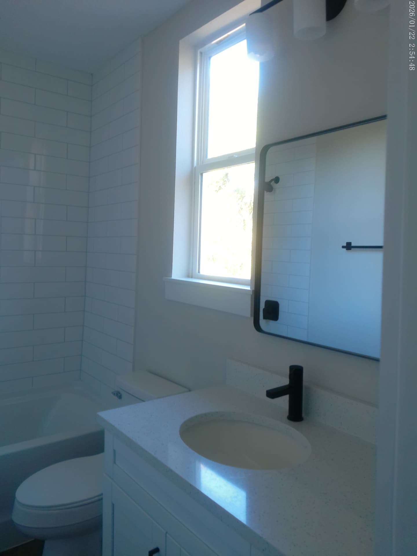Finished bathroom with subway tile tub surround, quartz vanity, and matte-black fixtures