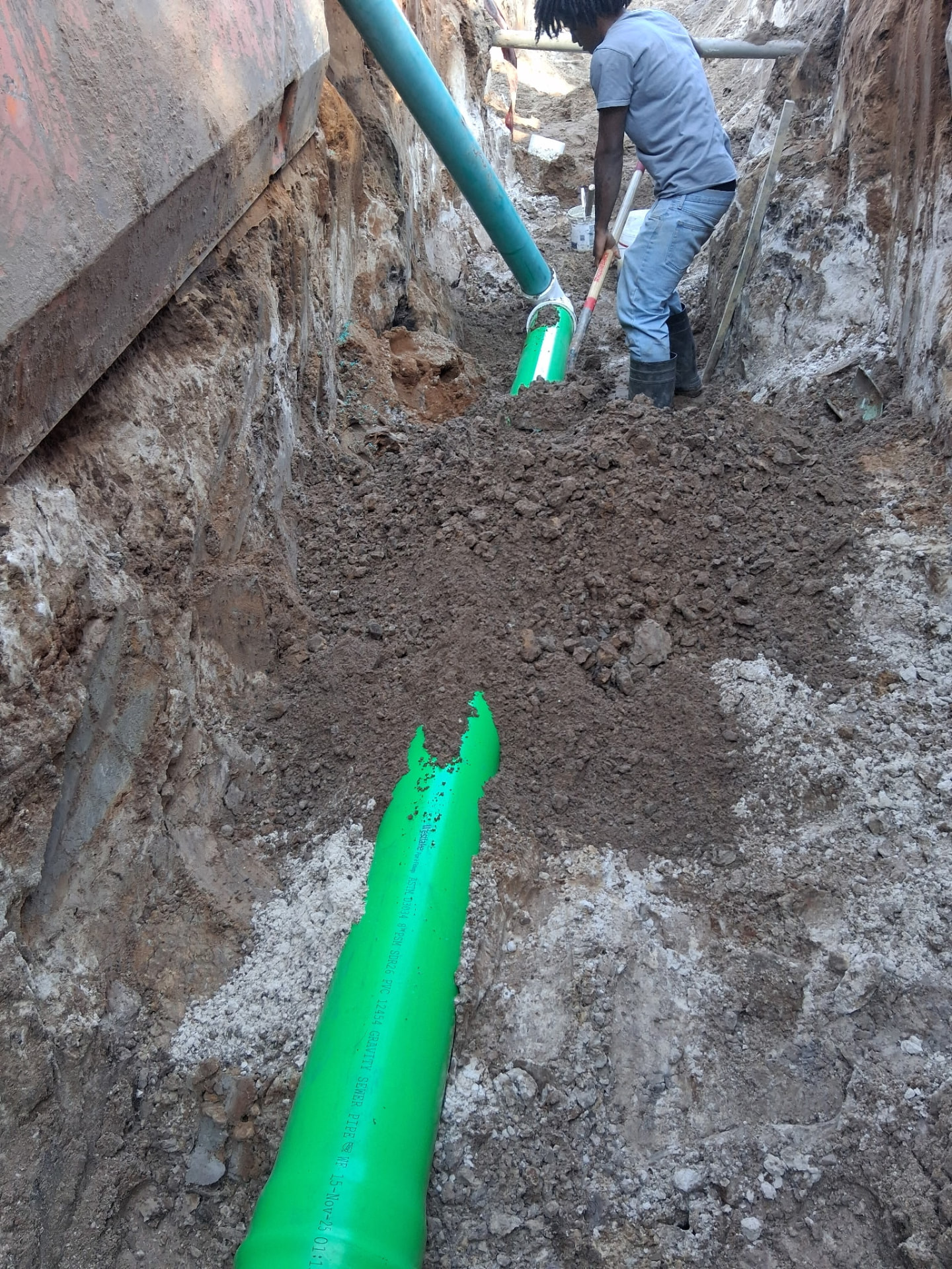 Spencer C&E crew member bedding green gravity sewer pipe in a shored trench