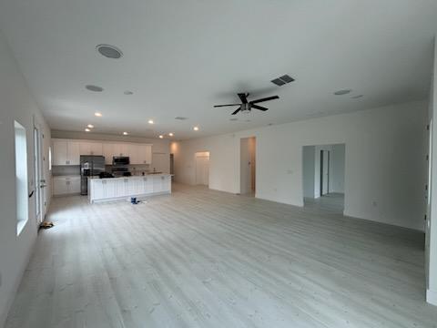 Open great room with light wide-plank flooring and view into the finished kitchen