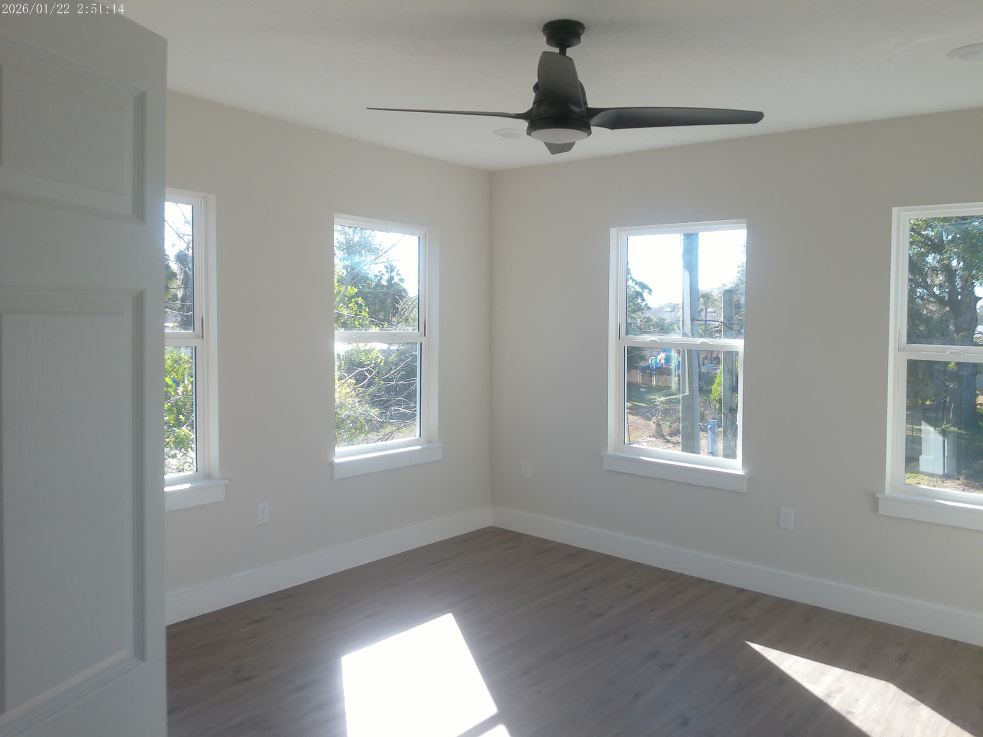 Finished corner bedroom with four windows, ceiling fan, and plank flooring